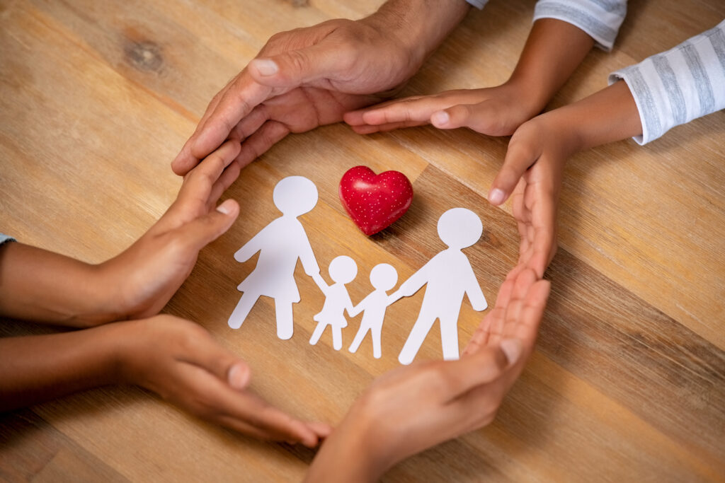 Multi-cultural hands surrounding paper cutout of family with a heart