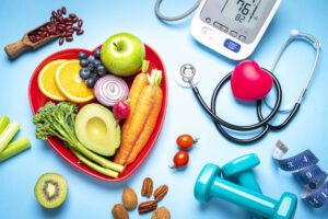 Healthy lifestyle concepts: red heart shape plate with fresh organic fruits and vegetables shot on blue background. A digital blood pressure monitor, doctor stethoscope, dumbbells and tape measure are beside the plate  This type of foods are rich in antioxidants and flavonoids that prevents heart diseases, lower cholesterol and help to keep a well balanced diet.