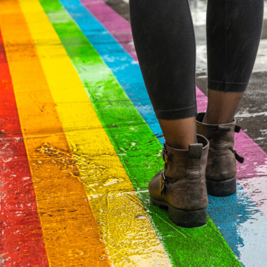Female legs walking on rainbow crosswalk in pride parade.