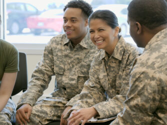 Male and female army soldiers sitting in a circle smiling and talking.