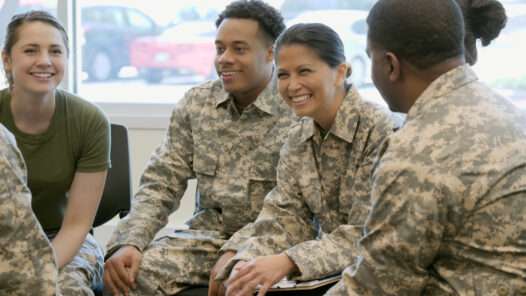 Male and female army soldiers sitting in a circle smiling and talking.