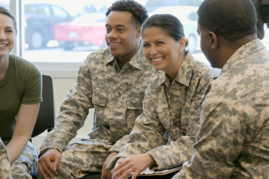 Male and female army soldiers sitting in a circle smiling and talking.