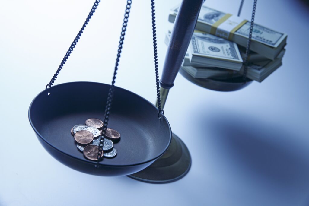 Scale with stack of dollar bills on one side and stack of change on the other.