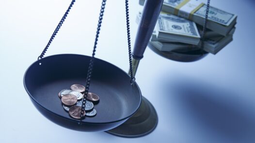 Scale with stack of dollar bills on one side and stack of change on the other.