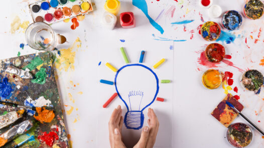 Hand drawn lightbulb with colorful paints over white paper.