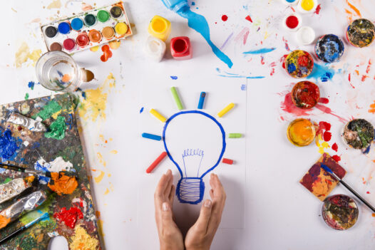 Hand drawn lightbulb with colorful paints over white paper.