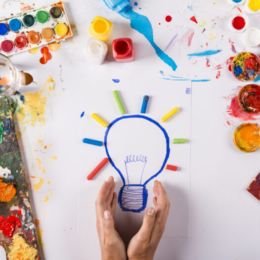 Hand drawn lightbulb with colorful paints over white paper.