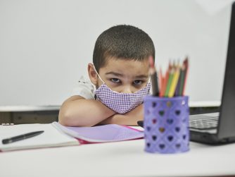 Young stressed out student wearing a mask staring at a laptop