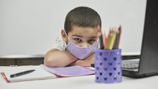 Young stressed out student wearing a mask staring at a laptop