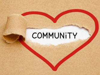 Handwritten word Community appearing behind torn red heart on brown paper.