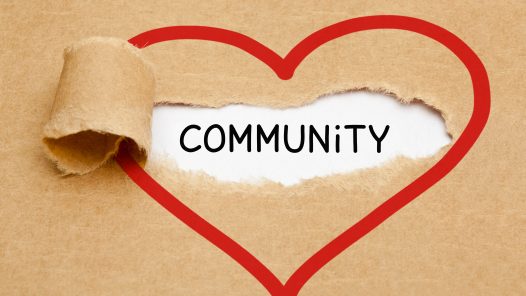 Handwritten word Community appearing behind torn red heart on brown paper.