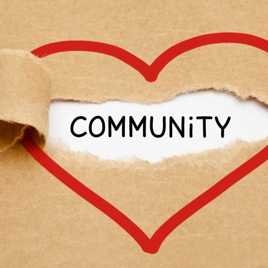 Handwritten word Community appearing behind torn red heart on brown paper.