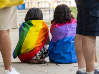 LGBTI, a couple enveloped in LGBT and bisexual flags at the gay pride parade