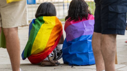 LGBTI, a couple enveloped in LGBT and bisexual flags at the gay pride parade