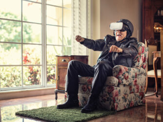 Old man sitting in an arm chair wearing a leather jacket, motorcycle helmet and VR headset.