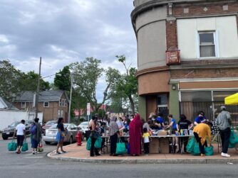 Street corner in city of Buffalo. People lining up at tables for food distribution.