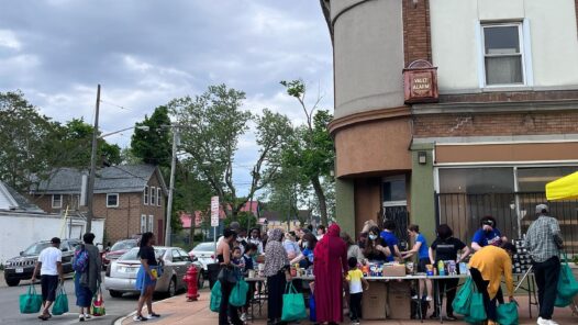 Street corner in city of Buffalo. People lining up at tables for food distribution.