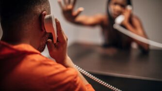 Incarcerated black male talking to spouse on prison phone.