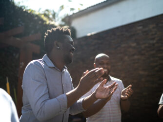 Black men in a circle clapping and smiling in community.