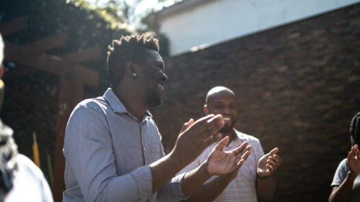 Black men in a circle clapping and smiling in community.