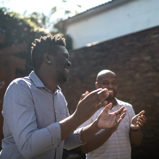 Black men in a circle clapping and smiling in community.