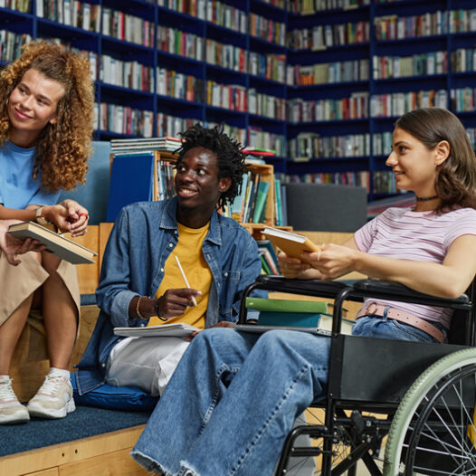 Diverse college students sitting in a circle on high benches talking. One female sitting in a wheel chair.