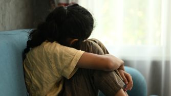 Child crying sitting on couch holding a stuffed animal for support/