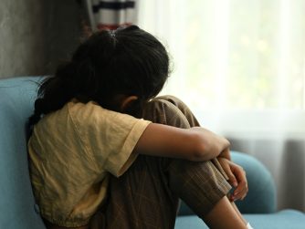 Child crying sitting on couch holding a stuffed animal for support/