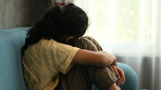Child crying sitting on couch holding a stuffed animal for support/