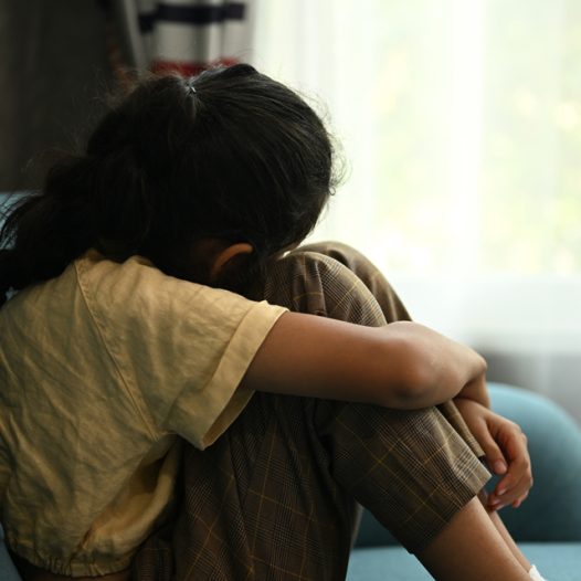 Child crying sitting on couch holding a stuffed animal for support/